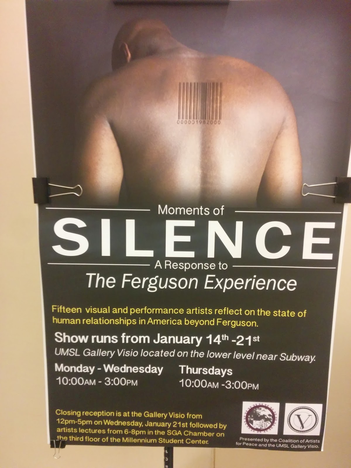 Photograph of a poster for an on-campus art exhibit about Ferguson. The exhibit is entitled 'Moments of Silence: A Response to the Ferguson Experience,' and the poster features a dramatic photograph of a black man's back, marked with a barcode. The poster notes that the artists featured, both visual and performing, will 'reflect on the state of human relationships in America beyond Ferguson.' The text is white and yellow.