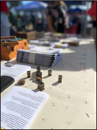 A photograph of a table view of a stack of zines, stamps, and paper at a book festival.